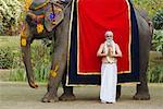 Priest standing in a prayer position beside an elephant