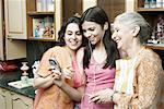 Three women standing in the kitchen and looking at a mobile phone