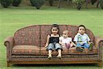 Three children sitting on a couch outdoors