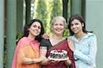 Portrait of a mature woman holding a cake with a young woman and a mid adult woman standing beside her