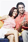 Young man holding a mobile phone with a young woman sitting on a couch