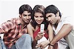 Gros plan d'une jeune femme et deux jeunes hommes regardant un téléphone mobile