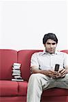 Close-up of a young man sitting on a couch operating a mobile phone