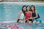 Portrait de trois jeunes femmes assis sur le bord d'une piscine