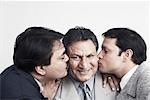 Close-up of two sons kissing their father