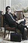 Portrait of a businessman sitting on an armchair holding a newspaper