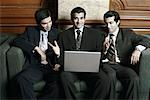 Three businessmen sitting on a couch with a laptop