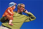 Low angle view of a mature man carrying a baby girl and talking on a mobile phone