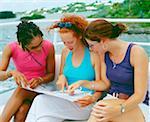 Close-up of three young women sitting on a bench and looking at a map, Bermuda