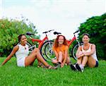 Porträt von drei jungen Frauen sitzen auf dem Rasen vor der Fahrräder, Bermuda