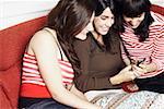 Two young women and a mid adult woman sitting on a couch and looking at a mobile phone