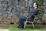 Side profile of a businessman sitting on a chair in front of a stone wall