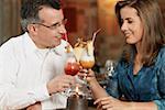 Close-up of a mid adult couple sitting in a restaurant and toasting glasses of pina colada