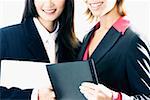 Close-up of two businesswomen holding files and smiling