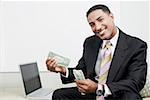 Portrait of a businessman sitting beside a laptop and counting paper currency