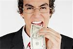 Portrait of a businessman putting a dollar bill into his mouth