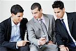 Gros plan de trois hommes d'affaires, assis et regardant un téléphone mobile