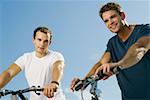 Portrait de deux jeunes hommes souriant et tenant des bicyclettes