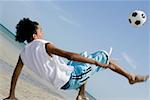 Rear view of a teenage boy playing with a soccer ball on the beach