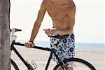 Mid section view of a man standing and holding a bicycle on the beach