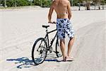 Rear view of a man standing and holding a bicycle on the beach