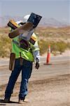 Rear view of a construction worker carrying hand tools on his shoulder