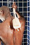 Rear view of a man scrubbing his back with a back brush