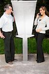 Side profile of a mid adult couple talking on pay phones