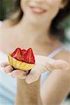Gros plan d'une jeune femme tenant une tarte aux fraise et souriant