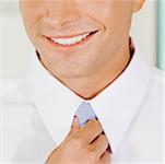 Close-up of a businessman adjusting his tie and smiling