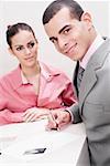 Portrait of a businessman writing on paper and a businesswoman standing beside him