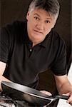 Portrait of a senior man holding a frying pan in the kitchen