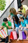 Three teenage girls and two young men sitting on steps and looking into shopping bags