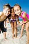 Portrait of two girls and a boy standing on the beach and smiling