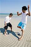 Two teenage boys playing with a soccer ball on the beach