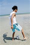 Rear view of a teenage girl playing with a soccer ball on the beach