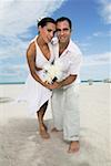 Portrait d'un jeune couple de danse sur la plage et tenant des fleurs