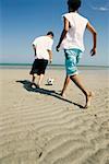 Rear view of two boys playing with a soccer ball on the beach