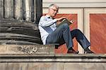 Man Sitting and Reading Book at Base of Column