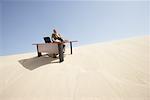 Homme d'affaires au bureau en haut d'une Dune de sable