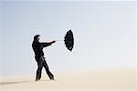 Homme d'affaires dans le désert avec parapluie balayées par le vent