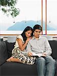 Couple Sitting on Sofa Reading Book Together