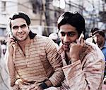 Two young men sitting in a rickshaw and talking on mobile phones