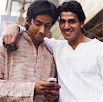 Portrait d'un jeune homme souriant avec un autre en utilisant un téléphone mobile