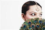 Gros plan d'une jeune femme tenant un fan de plumes de paon sur son visage