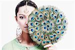 Portrait of a young woman holding a peacock feather fan over her face