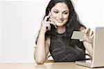 Close-up of a young woman talking on a mobile phone in front of a laptop