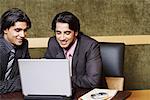 Two businessmen sitting in an office and using a laptop