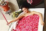 Erhöhte Ansicht einer jungen Frau in einer Badewanne voller Rosenblüten liegend