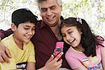 Close-up of a mature man and his grandchildren looking at a mobile phone
